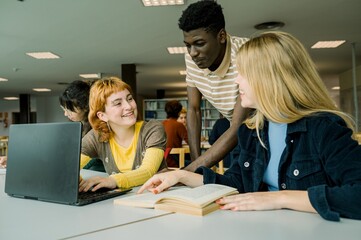 Diverse students sitting in library with laptop