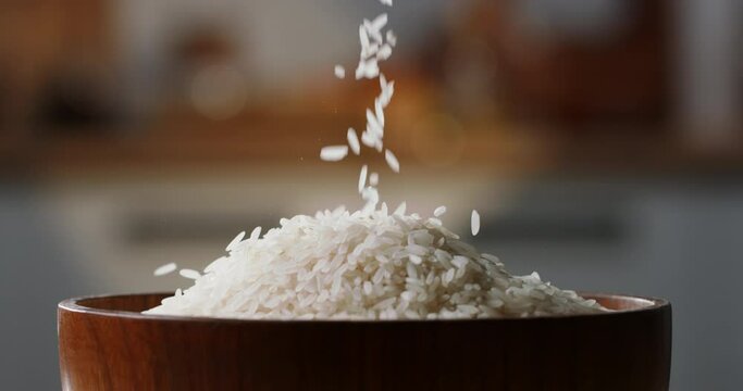 Rice being poured raw wooden bowl side view home kitchen blurred background White rice poured drop down, close up, organic Asian Indian Japanese Chinese food cuisine culture carbohydrate