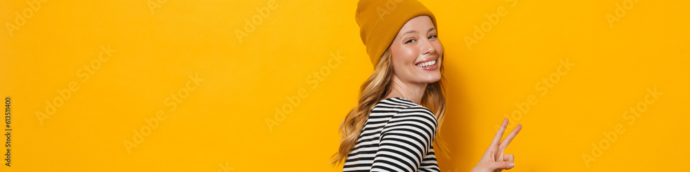 Wall mural Young blonde woman wearing hat smiling and gesturing at camera