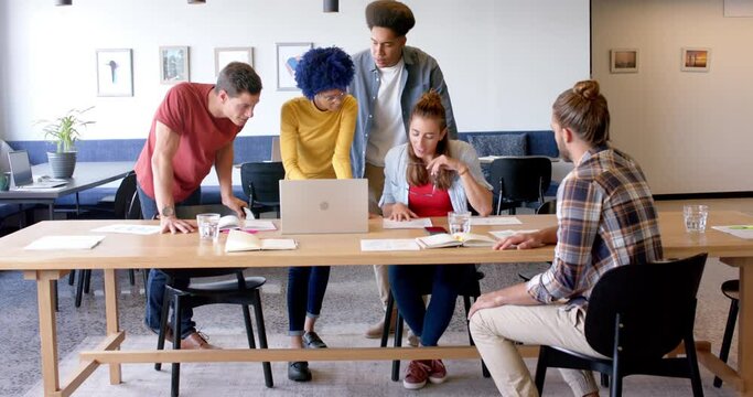 Portrait of happy diverse business creatives using laptop in discussion in office, slow motion