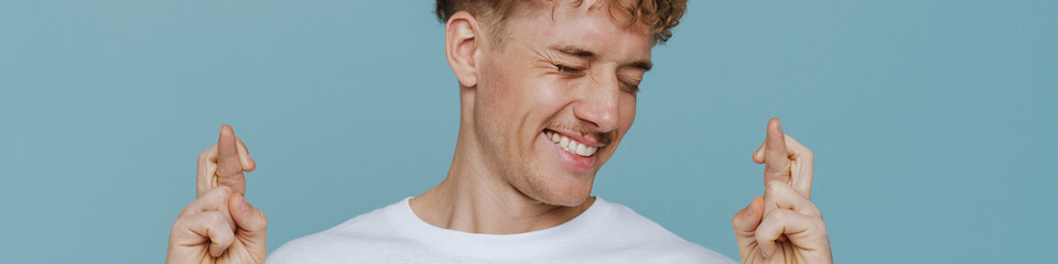 Obraz premium Young handsome hopeful man with closed eyes and crossed fingers