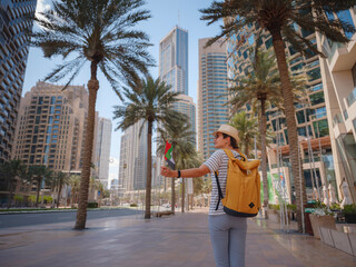 Enjoying travel in United Arabian Emirates. Young woman with yellow backpack walking on Dubai Downtown in sunny summer day. view from the back or rear view