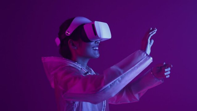 Woman in futuristic costume. Girl in glasses of virtual reality while touching air. Augmented reality game, future technology, AI concept. VR. Neon blue and red light. Dark background.