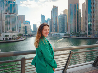 Fototapeta na wymiar young woman in green suit walks streets of Dubai, Dubai Marina district. United Arab Emirates trip concept. the idea of successful expat, moving to another country, work visa