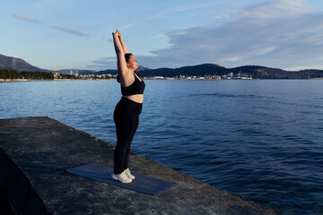 Young overweight girl does physical exercises on the seashore