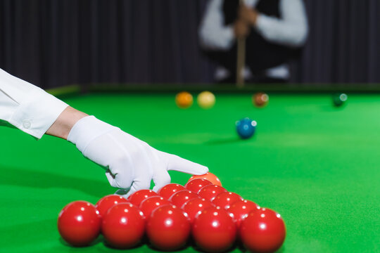 A snooker referee holds a pink ball at the start of the game. wearing white gloves