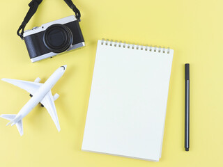 flat lay of blank page opened notebook with pen, airplane model and digital camera on yellow  background with copy space.