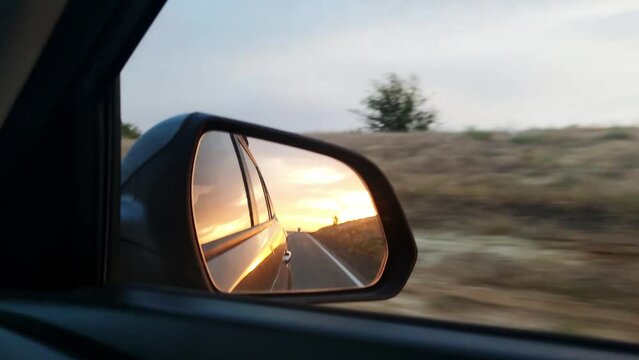 Sunset view in the side view mirror of a car driving on the road in the field.