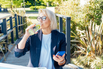 Healthy habit to drink water. Smiling middle aged business woman with bottle of water with lemon and mint during her outdoor lunch break. Control body hydration, Tracker water balance. Healthy living