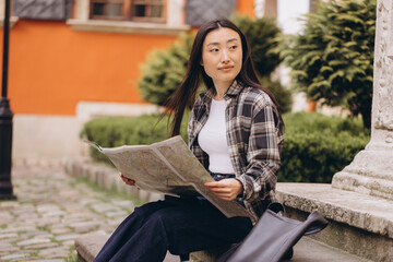 Portrait of a beautiful happy brunette Korean woman holding a map on the streets of the old city. Asian woman tourist lady traveling in Europe.