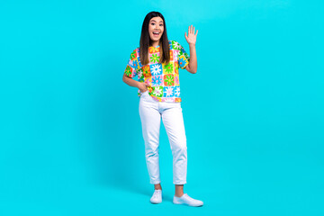 Full body cadre of positive friendly japanese hipster girl wear trendy clothes wave hand hello sign isolated on aquamarine color background