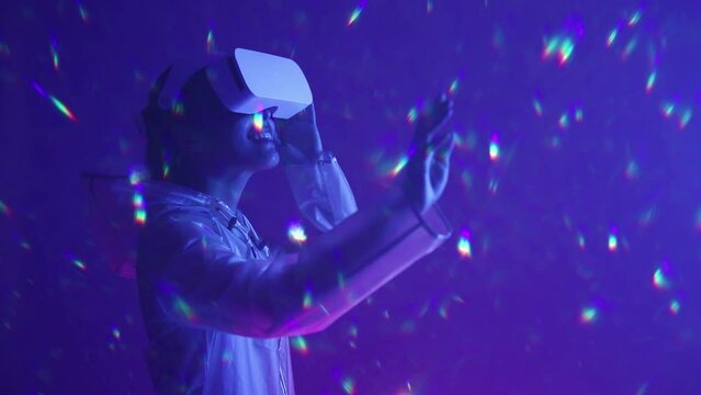 Woman in futuristic costume. Girl in glasses of virtual reality while touching air. Augmented reality game, future technology, AI concept. VR. Neon blue and red light. Dark background.