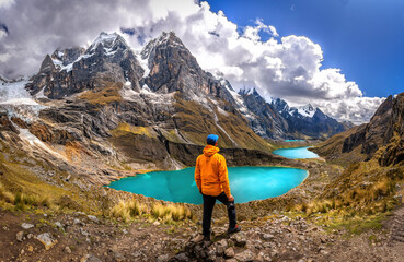 Man standing in front of a teal water lake with high Peruvian mountains in the Huayhuash mountain...