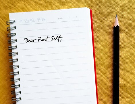 Notebook on yellow background with handwritten text DEAR PAST SELF, self reflection by writing a letter to person you were, advice to give past self to tell them about what happened then and now