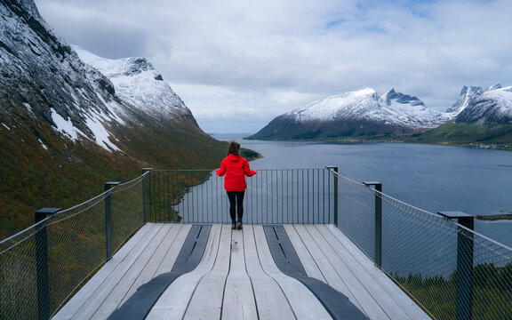 Female tourist stands at a viewpoint during the clear sky, Bergsbotn utsiktsplattform Is a viewpoint that overlooks the beautiful bay and mountains Located in northern Norway.