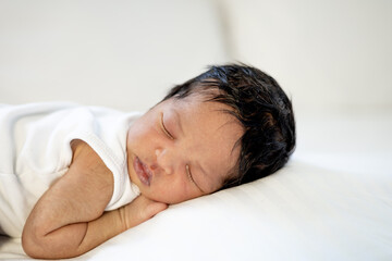a newborn black African-American baby is sleeping sweetly on his tummy, a small dark-skinned baby is lying on the bed in the bedroom in close-up