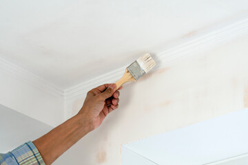 Apartment renovation. A hand with a brush paints the ceiling white