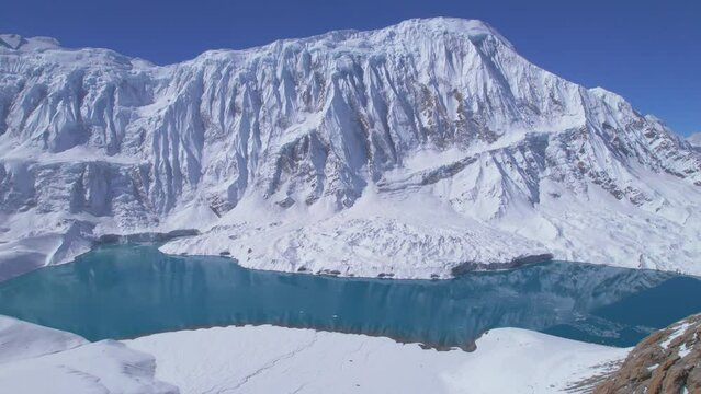 Aerial panning side view blue alpine big Tilicho lake surrounded by snowy Himalayas mountain range in Nepal. Manang. Highest Alpine lake on earth concept