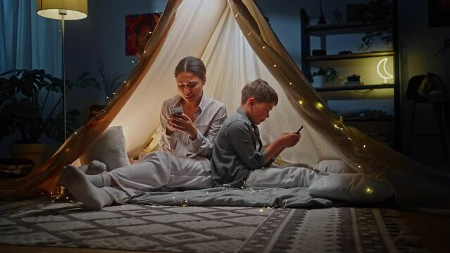 Full length portrait young woman mother and child son playing online video games inside a game tent