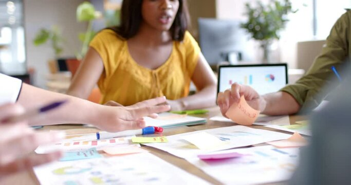 Happy diverse colleagues brainstorming with documents and tablet at table in office in slow motion