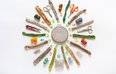 Concept of hand embroidery. Circular composition of accessories for cross stitch: hoop with canvas, scissors, set of needles, skeins of cotton threads in natural colors, pins. Flat lay, close-up