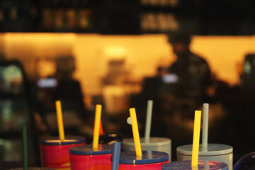 Colorful cups and straws create a vibrant foreground, framing a bustling café atmosphere