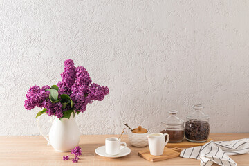 A modern kitchen countertop interior with items for morning coffee and a jug of lilacs, a gray textured wall with a replica of the space. Eco house.