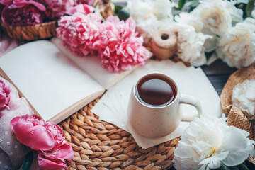 Beautiful spring composition, good morning concept. Cup of tea, peonies and open book