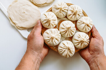 male hands cook hold round wooden board with khinkali