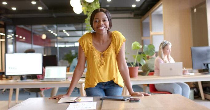 Portrait of happy african american casual businesswoman standing in office smiling, slow motion