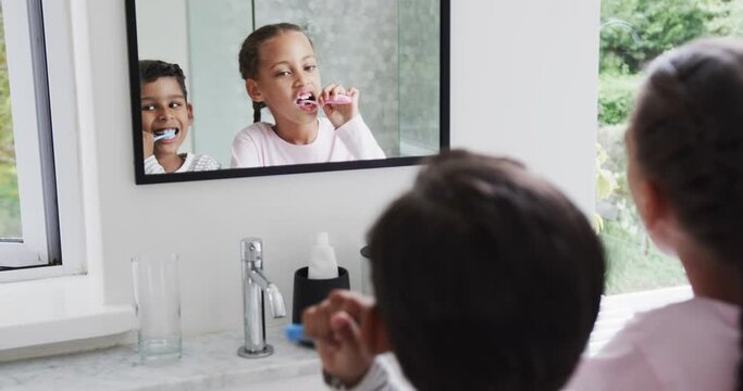 Happy biracial brother and sister brushing teeth in sunny bathroom, slow motion