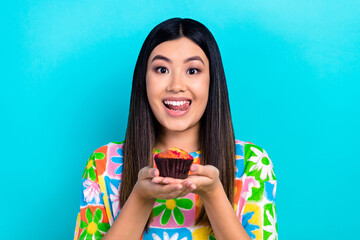 Photo of hungry shiny woman dressed flower print t-shirt eating tasty cupcake licking lips isolated blue color background