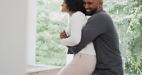Happy biracial couple brushing teeth in sunny bathroom, slow motion