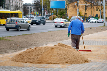 Pile of sand lies on new sidewalk, man seal seams between paving slabs. Laying of paving slabs....
