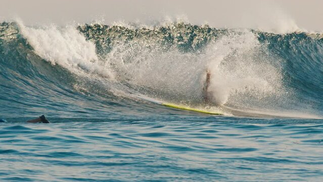 Man surfs the wave in the Maldives at sunset and falls