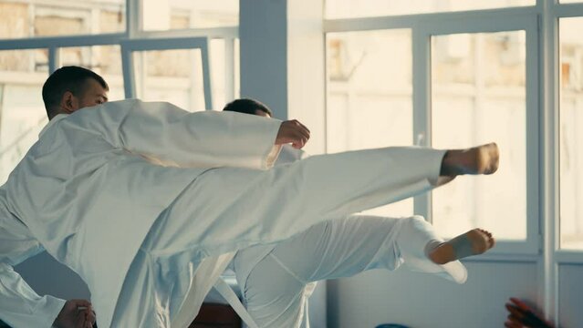 Two men in white uniforms synonymously kicking air, taekwondo training, sport