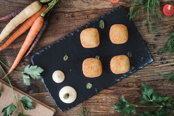 delicious fried mozzarella cheese balls served on a black ceramic plate, fresh vegetables on a wooden rustic table