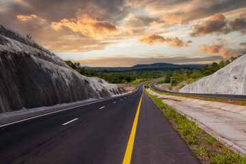 Aerial view of mountain road in forest at sunset in autumn. Top view from drone of road in woods. Beautiful landscape with roadway in hills, pine trees, green meadows, golden sunlight in fall. Travel