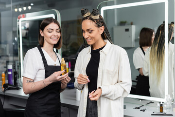 client satisfaction, hairdresser suggesting hair oil to female customer, happy woman with braids, hairstyle, hair buns, braided hair, beauty salon, hairstyling product