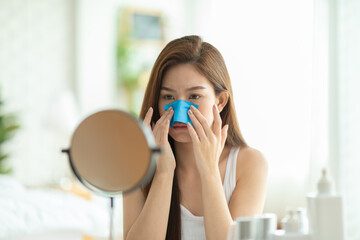 Asian young woman looking in mirror doing skin care touch cheek using oil film worry about oily face and beauty treatment at home,Wellness woman self care with beauty product at home - obrazy, fototapety, plakaty