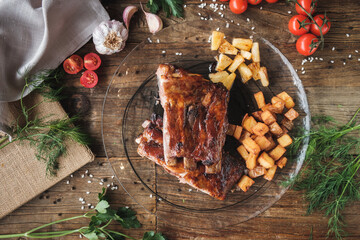 grilled ribs with vegetables, baked potatoes and pineapple on a glass plate, wooden table, top view, fresh ingredients around