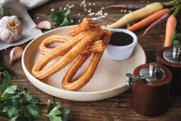 Fresh baked sweet churros with chocolate sauce on a plate on rustic wooden table, ingredients surrounding the plate