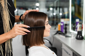 Fototapeta premium salon job, hairdresser with braids brushing hair of woman, professional hair comb, hairstyling, hair treatment, hairdo, extension, salon customer, beauty profession, client satisfaction, side view