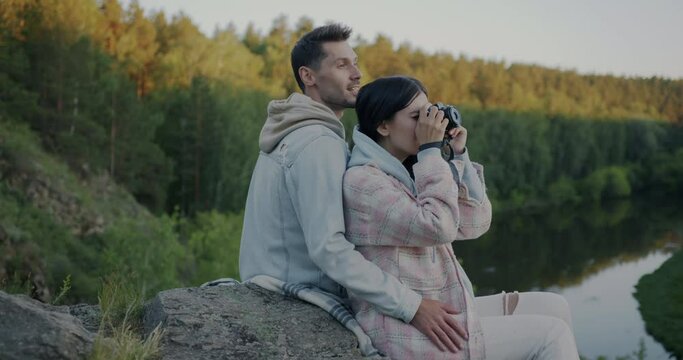 Slow motion of happy girl and guy taking photo with modern camera enjoying spectacular view of forest and river in mountains. Tourism and photography concept.