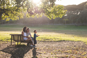 Cute white family spending time in the park - a little boy blowing soap bubbles while his parents sitting on a bench