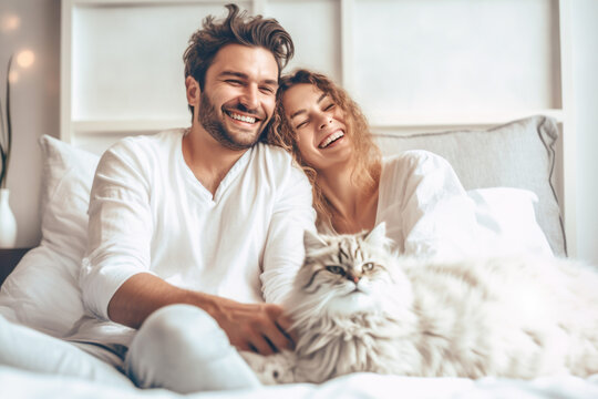 Happy smiling couple and their shaggy cat sitting on the bed, enjoying relaxed morning at home 