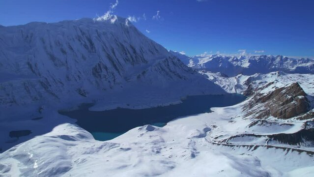 Aerial revealing view picturesque blue Tilicho lake surrounded by high altitude snowy Himalaya mountains range in sunny day. Tilicho base camp route, Manang, Nepal