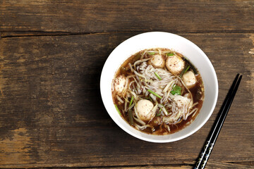 thai local blood noodle with meat balls called boat noodle is famous street food served on the wooden table with black chopsticks during lunch in the local noodle shop in Thailand
