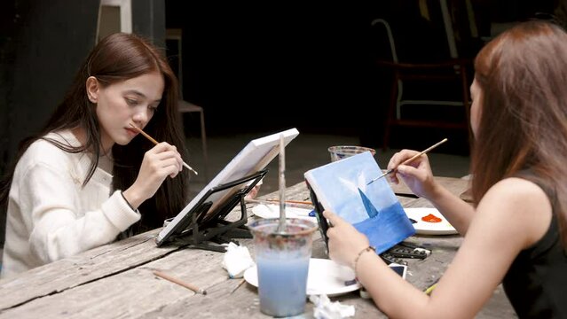 Two Asian teenagers learning to draw and paint In my spare time from studying. Woman holding a small paint brush Painting on white cloth to create a beautiful painting with intention