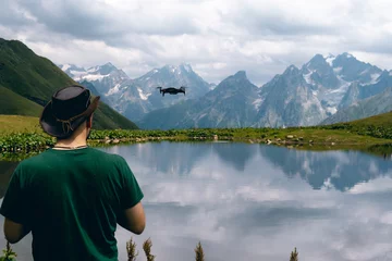 Fotobehang A man use small drone. Drone control, video recording and photography from the air. Unmanned aerial vehicle. Koruldi Lake Reserve. Mountains of the Caucasus. Georgia. Copy space © Sergey
